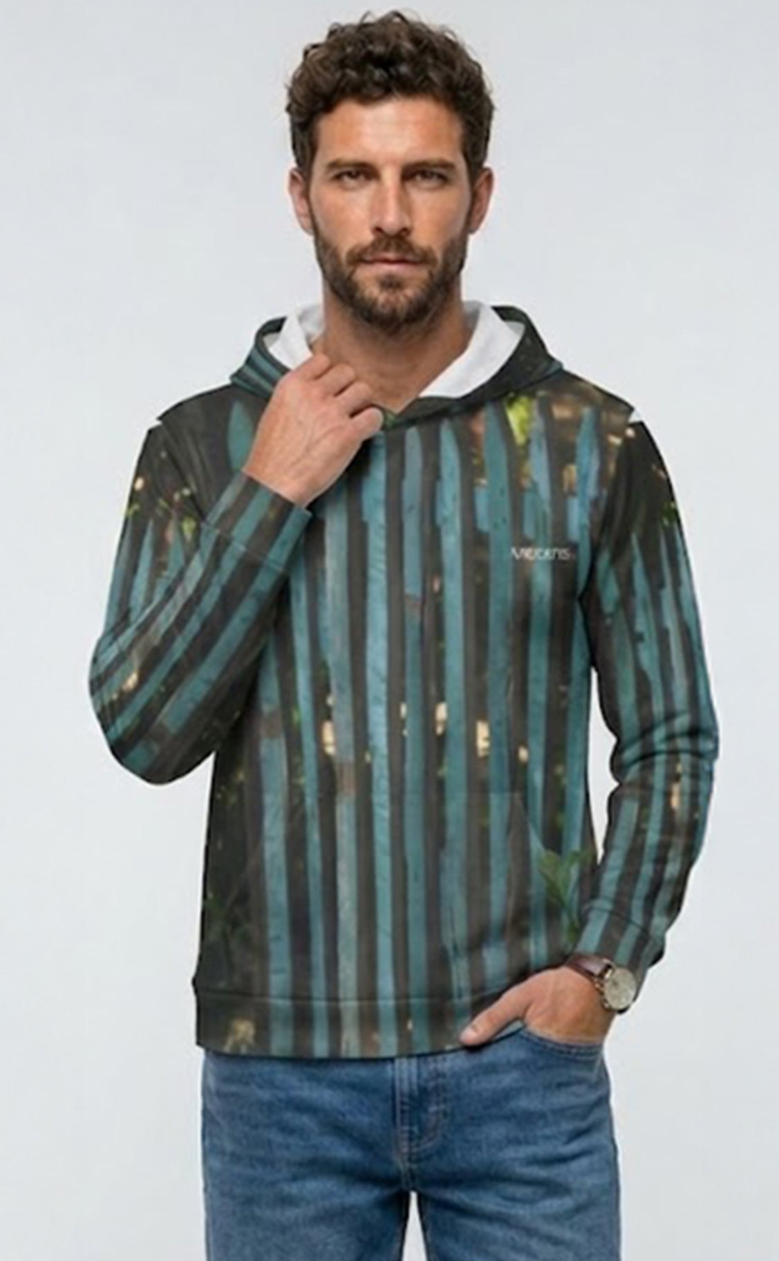 A man wearing a long-sleeve hoodie with vertical teal, green, and black stripes, featuring a white inner hood lining and a small white logo on the left chest, paired with blue jeans against a light gray background.