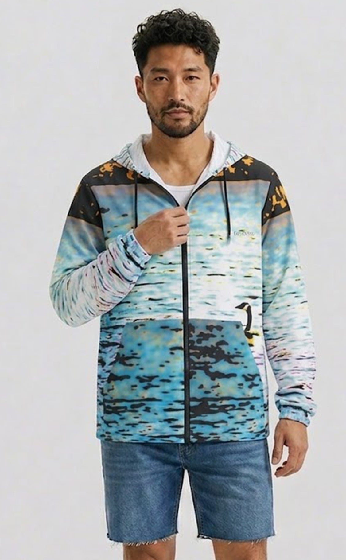 A man wearing a zip-up hoodie with a blue and black watercolor-style print, styled with blue denim shorts against a light gray background.