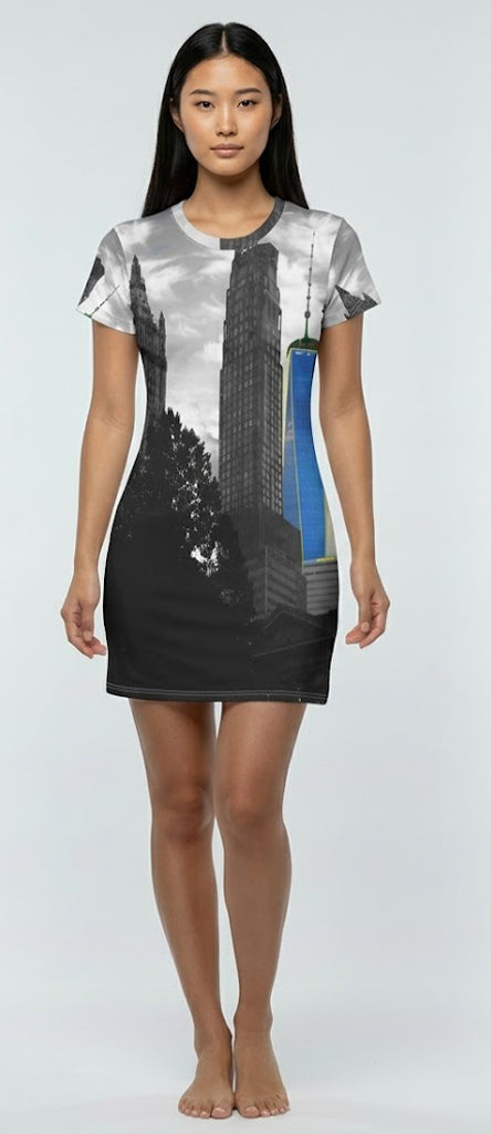A woman modeling a short-sleeve crewneck dress with an all-over cityscape print featuring black and white skyscrapers and a blue vertical accent, set against a plain light gray studio background.