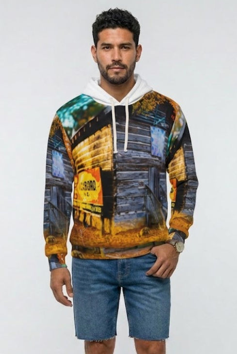 A man modeling a long-sleeve hoodie with a colorful, painterly abstract print in yellow, blue, and brown tones, paired with blue denim shorts and brown sandals, against a plain light gray background.