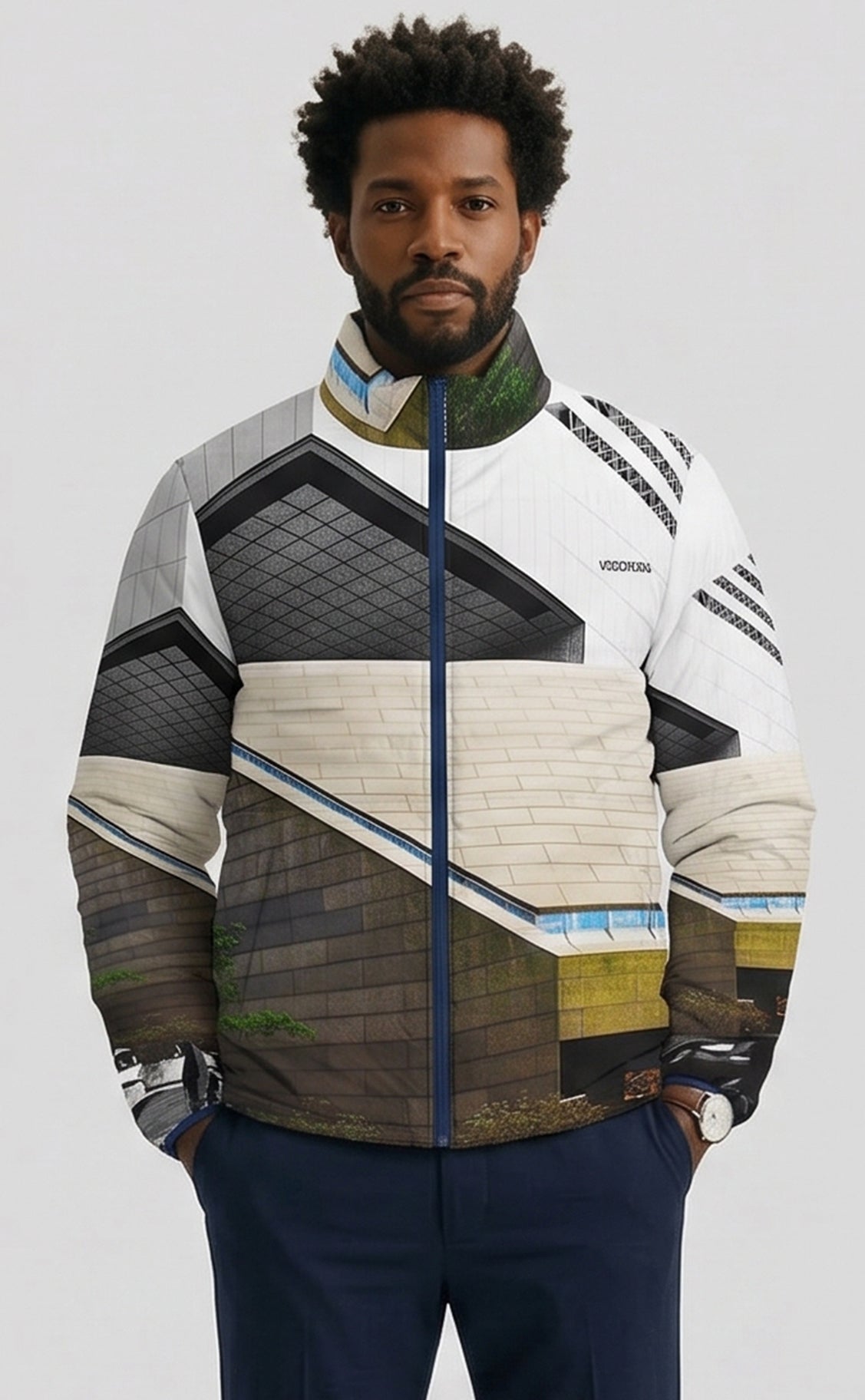 A man wearing a Vionnet puffer jacket with a complex architectural cityscape print, featuring white, gray, brown, and green sections, paired with navy pants against a light gray studio background.